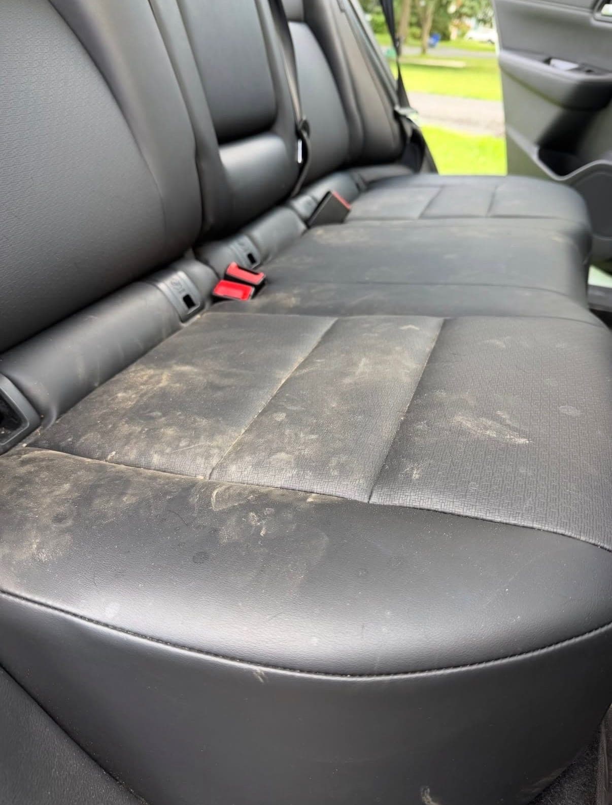A black leather rear bench seat before detailing, its surface dulled by dried-on dirt and dust